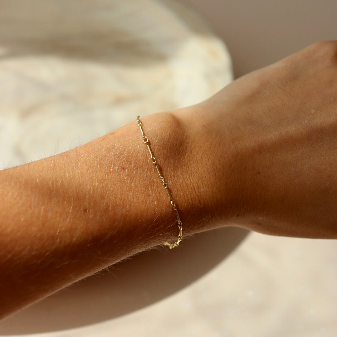Model wearing 14k gold fill dot + dash bracelet. This is a gold bar link chain. Model is wearing a light purple tank top. 