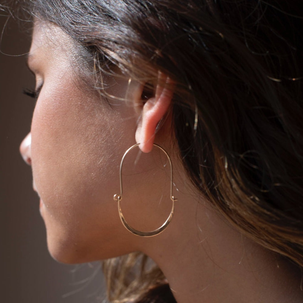 Model wearing Hammered Paloma Hoops. These earrings feature a wire around 1/2 inch shaped like an oval, then followed by the other half of the oval that is hammered.