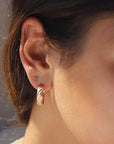 Brunette model wearing 14k gold fill cross studs. Model is also wearing gold ripple hoops. 