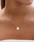 Brunette model wearing the westly monogram necklace. This necklace features a thin gold chain with a square stamped pendant with the letter "C."