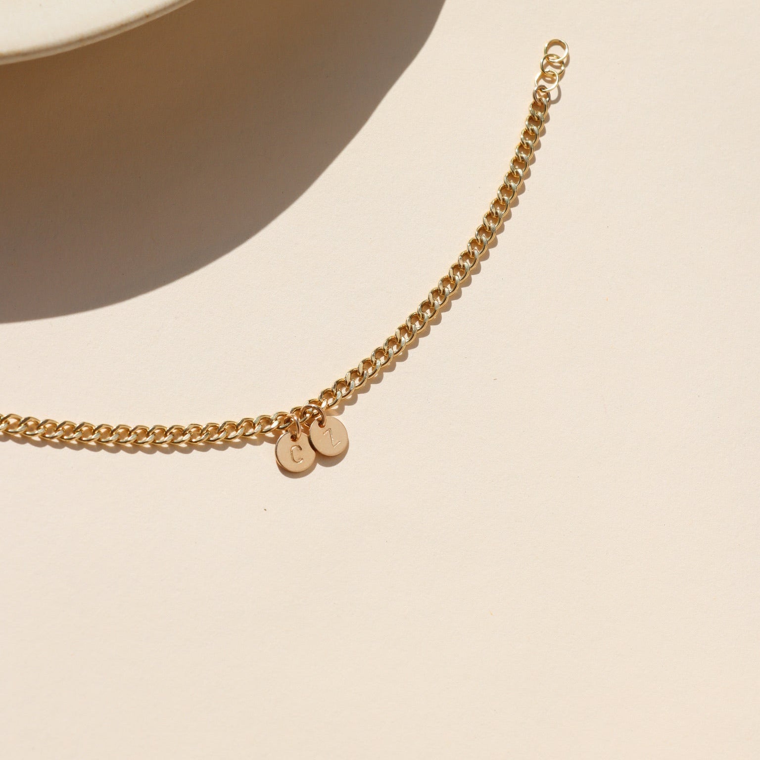 14k gold fill curb chain bracelet with hand stamped round disc charms on a light table