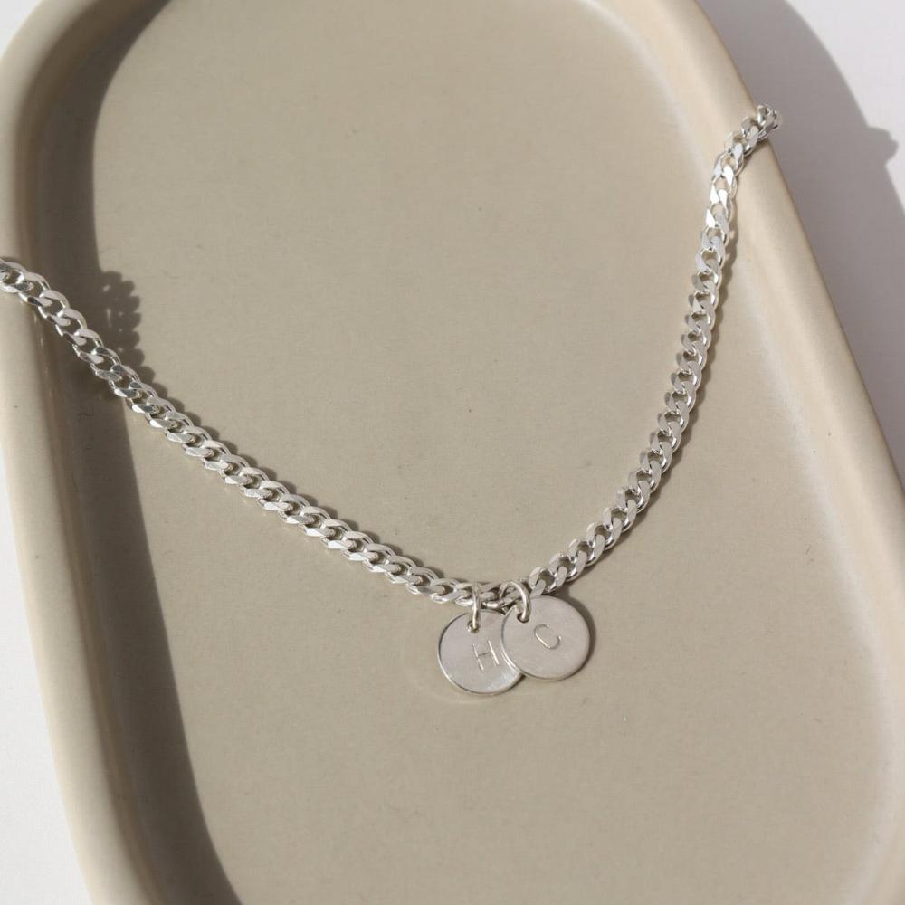925 sterling silver Modern Muse initial Necklace in sterling silver laid on a gray plate in the sunlight. This necklace feature the Carter chain with the choice of adding on an initial charm.