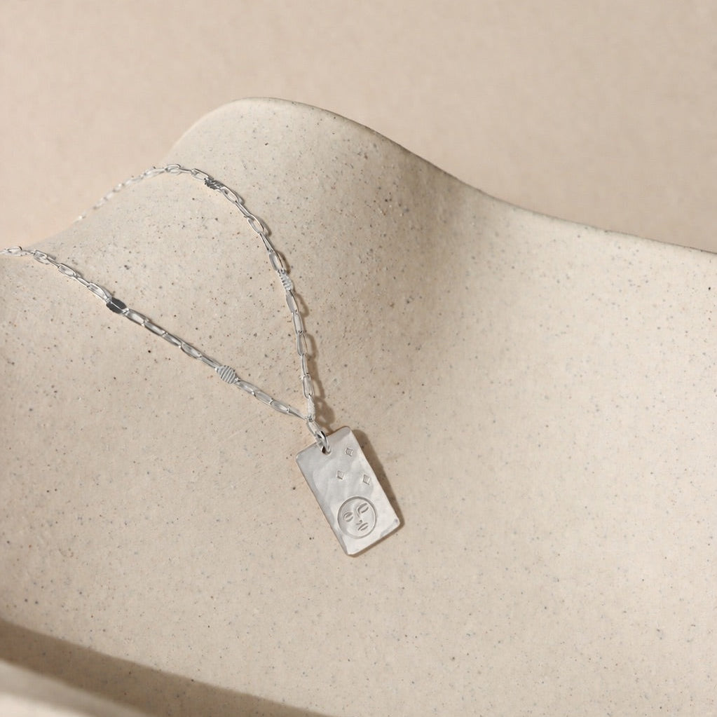 sterling silver chain necklace with hand stamped moon & stars pendant on a light dish