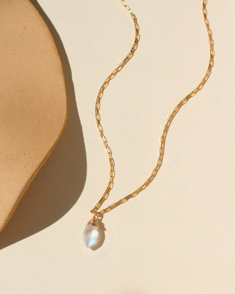 A 14k gold fill box chain featuring a Marquise Moonstone Gemstone wired wrapped at the end. Necklace is displayed on a cream back drop. 