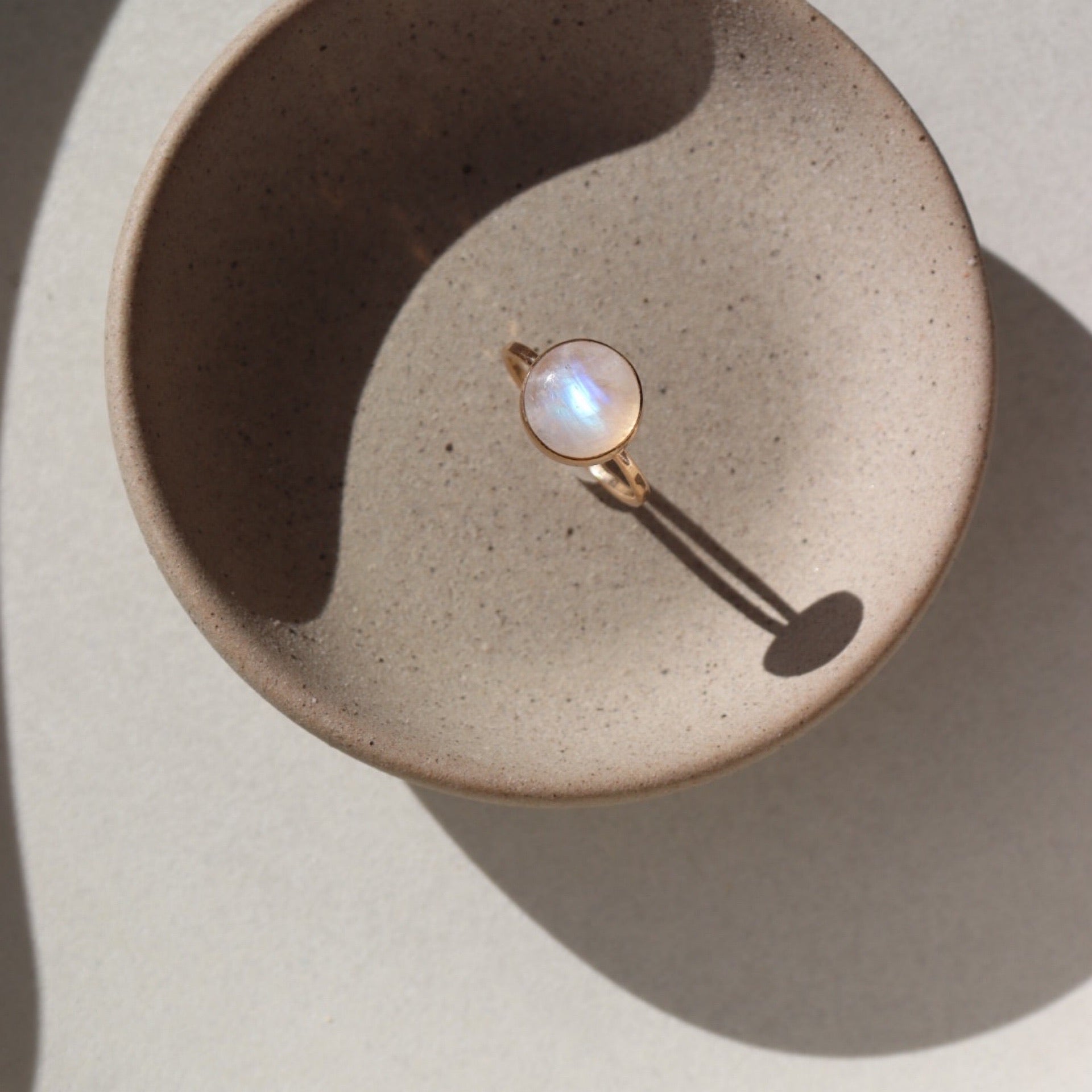 14k gold fill moonrise ring laid on a gray plate in the sunlight. This ring features a simple gold band with hammering and a moonstone