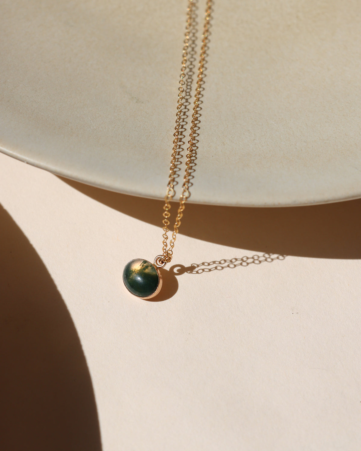 Oval deep green gemstone pendant necklace with a gold bezel and delicate gold chain.