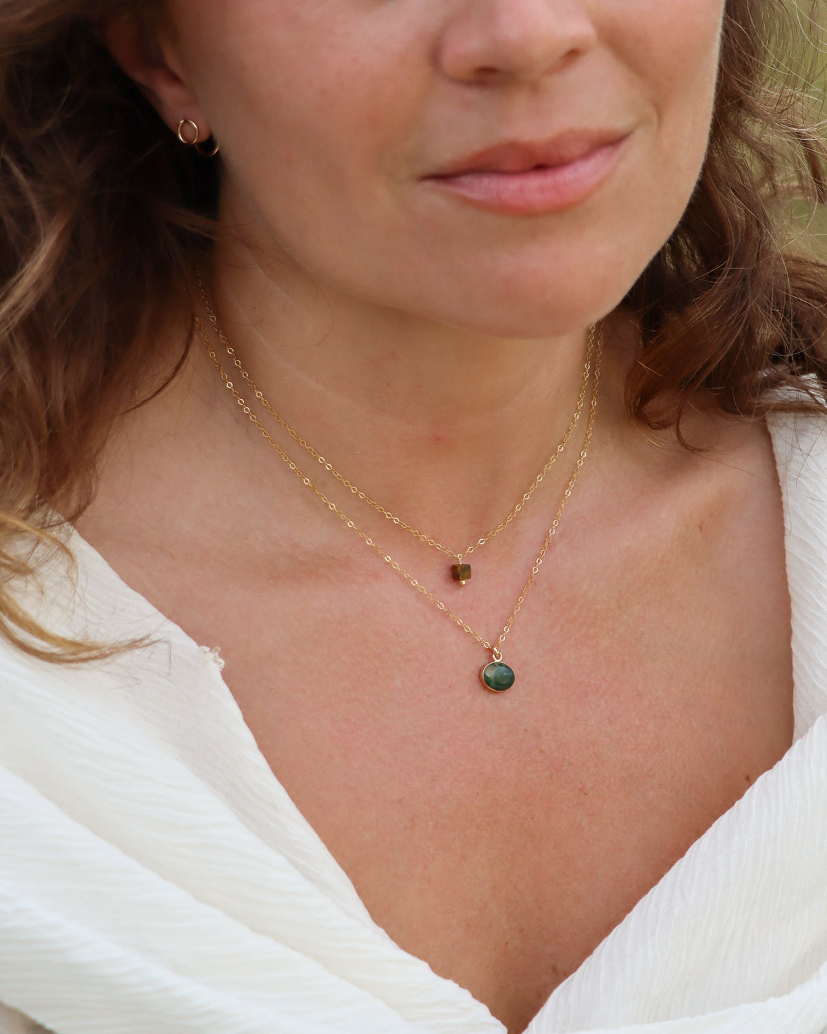 Oval green gemstone pendant necklace on a delicate gold chain, layered with a tiny brown gemstone necklace.