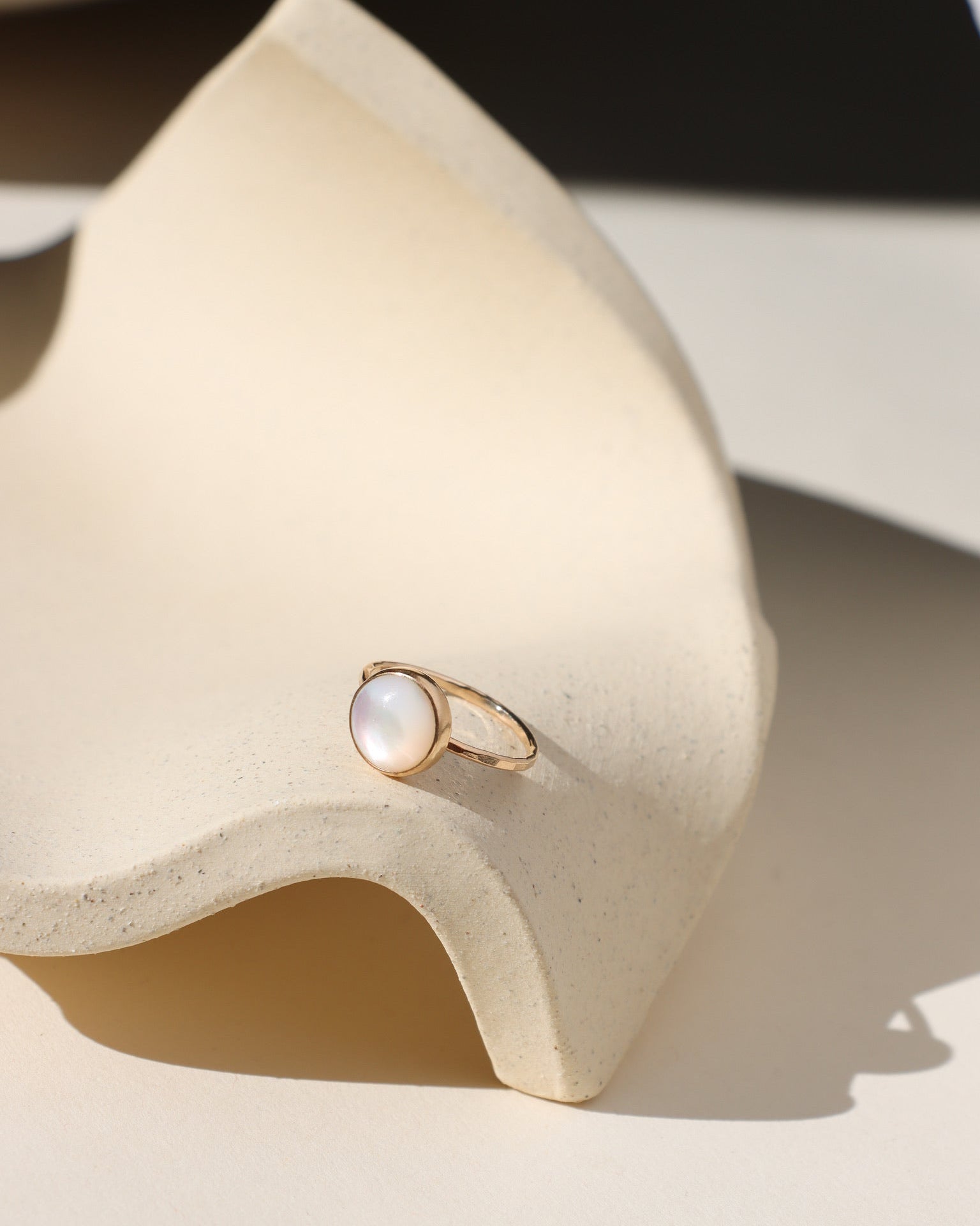 14k gold fill ring with round mother of pearl stone on a light dish