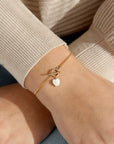 Model wearing the mother of pearl toggle bracelet. This bracelet features a gold curb chain with a toggle clasp opening with a mother of pearl heart at the end. 