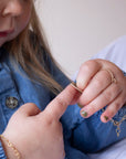 a young girl putting on a 14k gold fill spiral band with a tiny heart charm, and a heart chain bracelet