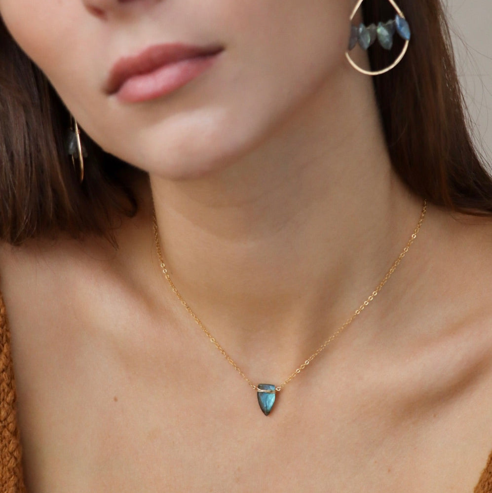Model wearing spear-shaped labradorite pendant on gold chain, handmade anniversary jewelry