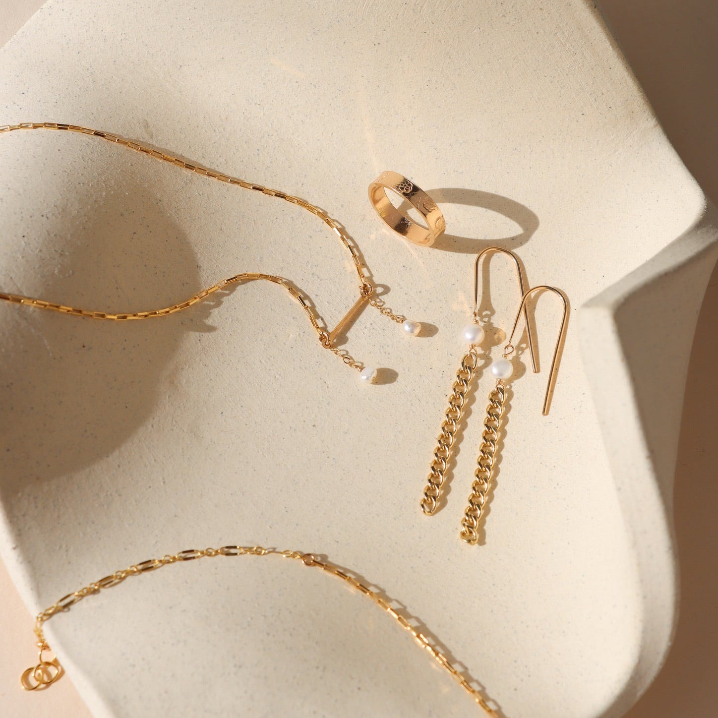 Gold jewelry including a necklace, ring, and earrings on a beige stone surface.