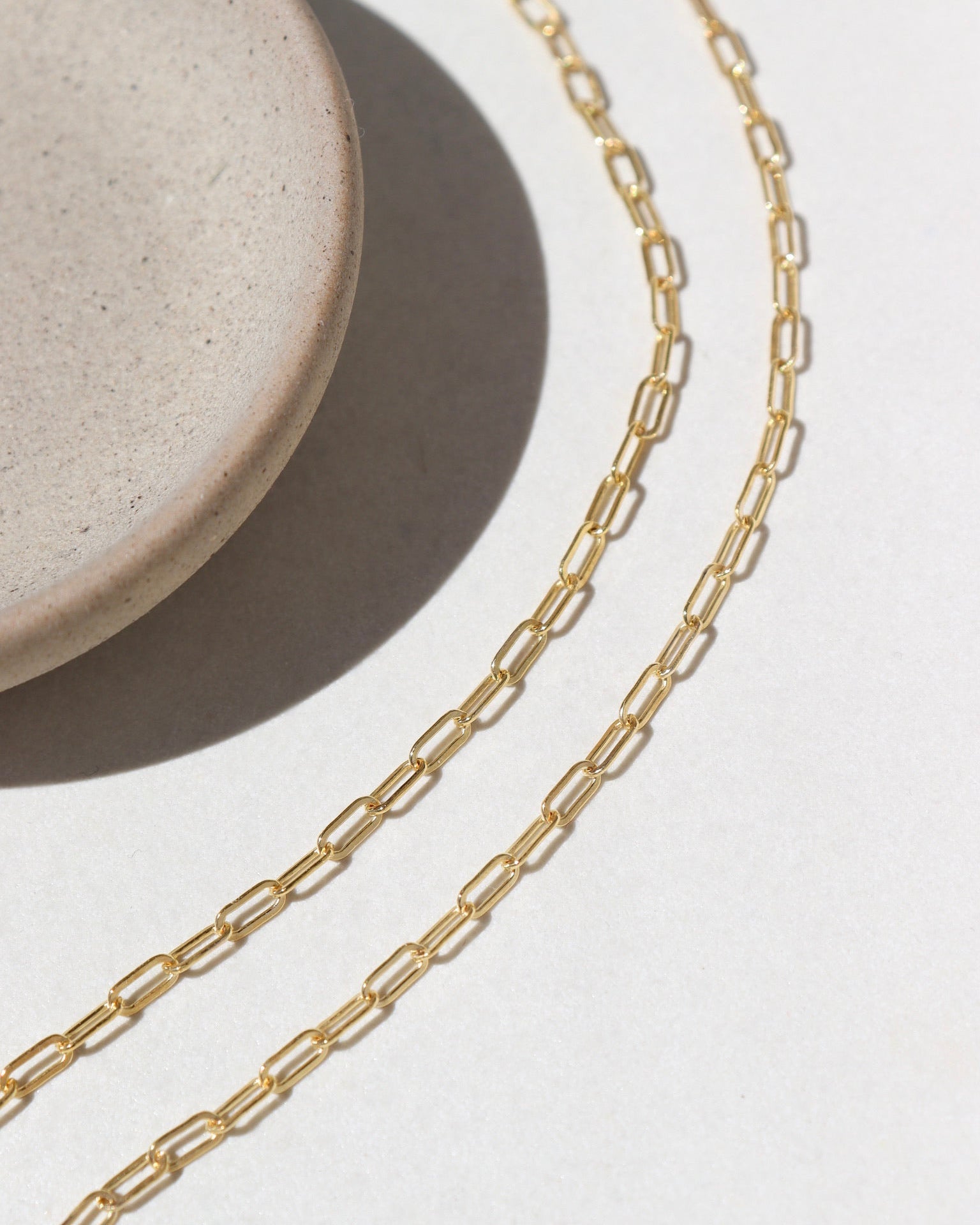 14k Gold fill Narrow Links chain laid on a white paper in the sunlight.