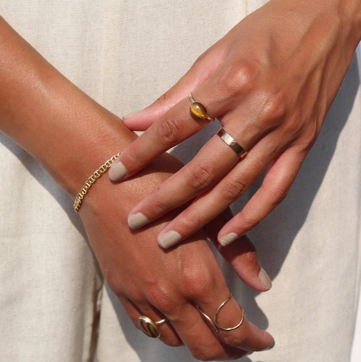 An amber-colored Tiger Eye gemstone on a horizontal bezel on a 14k gold fill band. Model wears this ring and other 14k gold fill wire rings by Token Jewelry