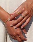 An amber-colored Tiger Eye gemstone on a horizontal bezel on a 14k gold fill band. Model wears this ring and other 14k gold fill wire rings by Token Jewelry