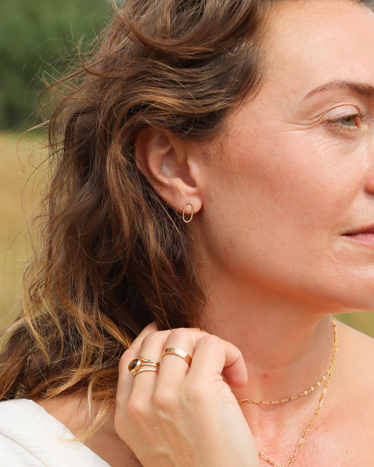 Gold-filled open oval stud earrings styled with layered gold necklaces and stacked rings.