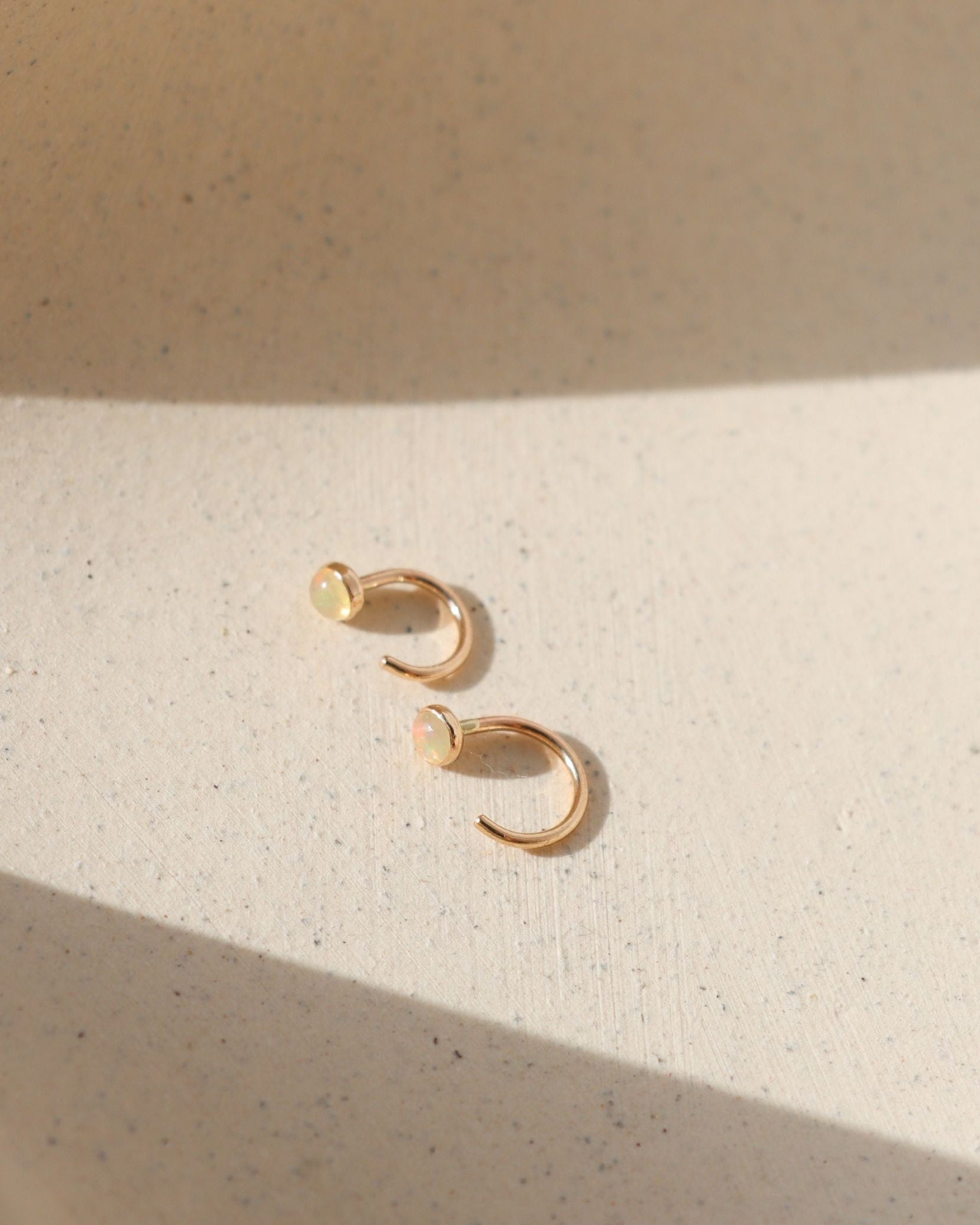 14k gold fill huggie style earrings with 3mm Ethiopian Opals on a light surface