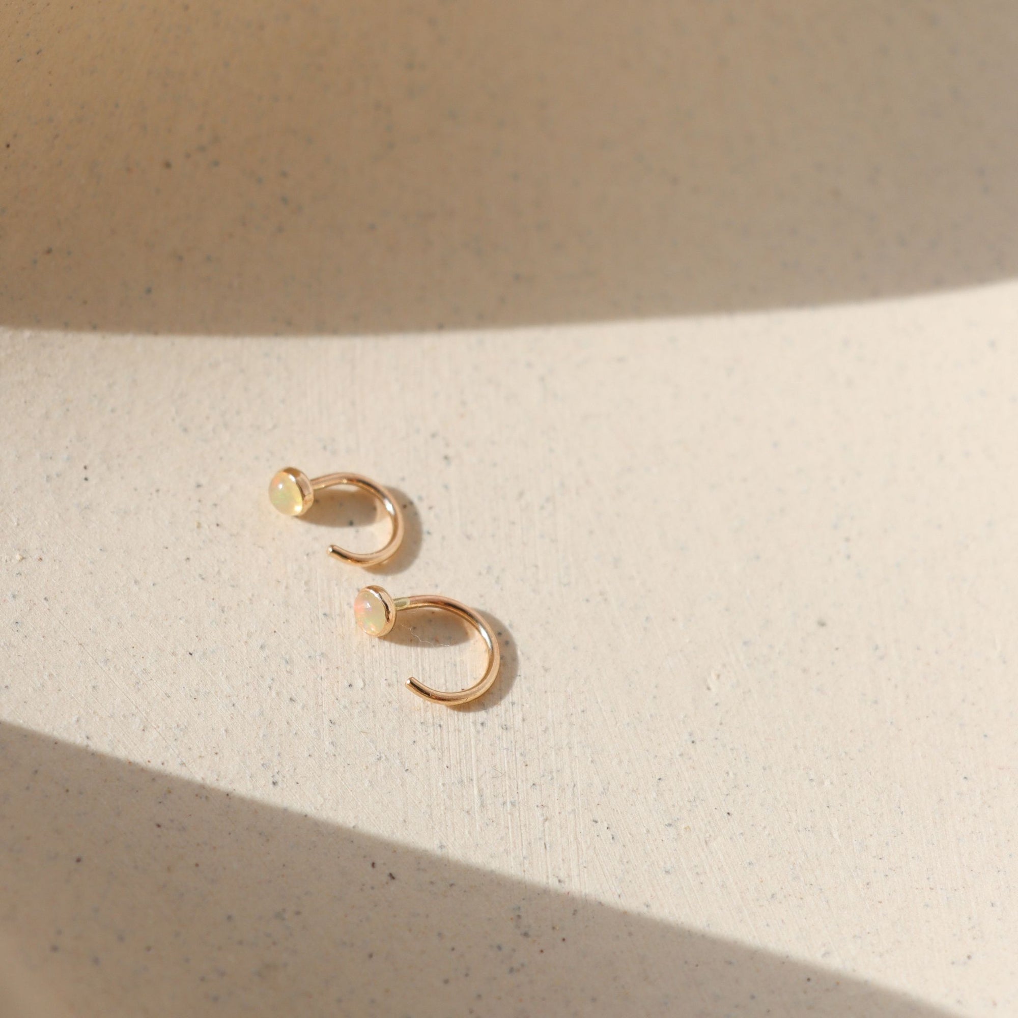 14k gold fill huggie style earrings with 3mm Ethiopian Opals on a light surface
