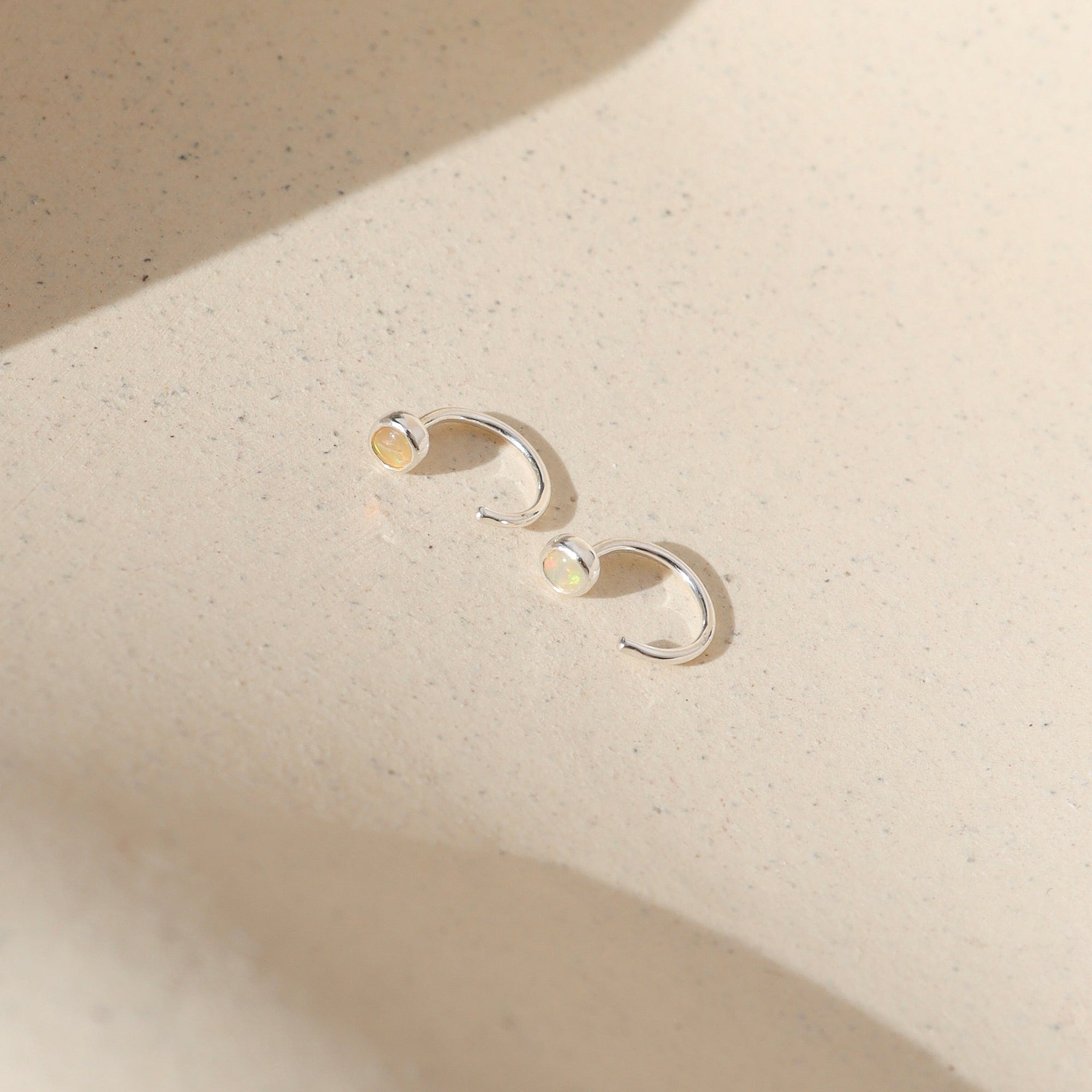 sterling silver huggie style earrings with 3mm Ethiopian Opals on a light surface