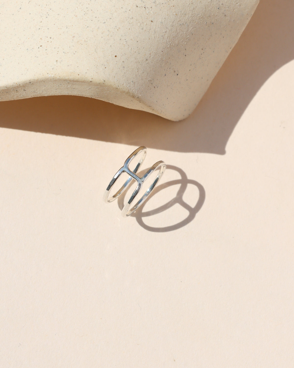 Sterling silver geometric open band ring displayed on a neutral surface in warm sunlight.