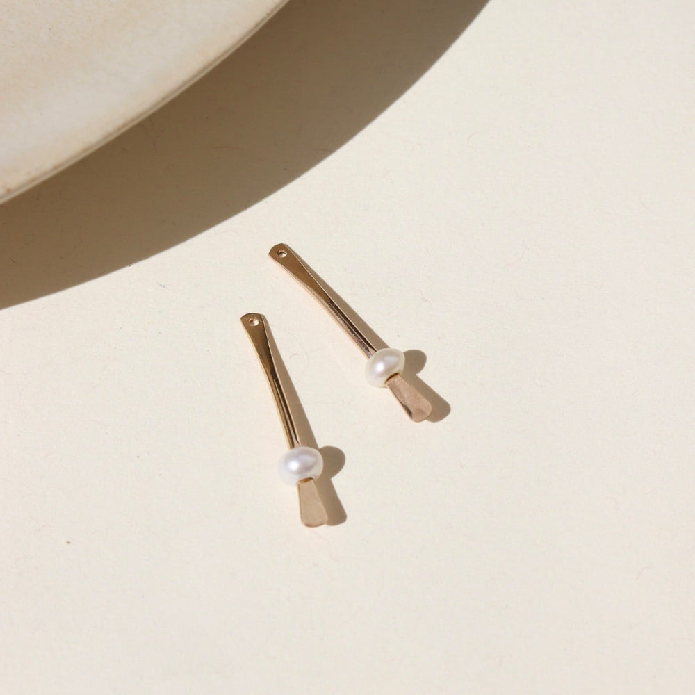 A 14k gold fill drop down post with a pearl on each ear jacket, the earrings are displayed on a cream back drop in the sunlight. 