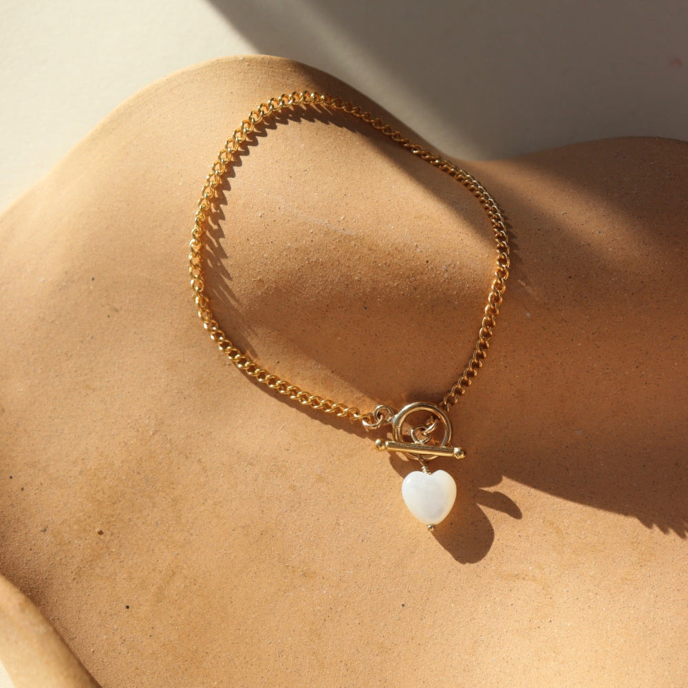 Bracelet by Token Jewelry - a 14k gold fill La Mer Chain with a toggle and a mother of pearl heart charm. This bracelet features a gold curb chain with a toggle clasp opening with a mother of pearl heart at the end. 