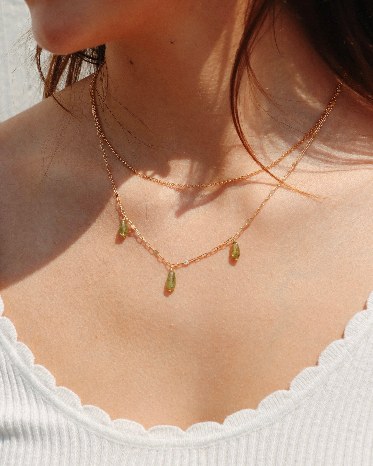 Model wearing a 14k gold fill Peridot Charm Necklace with three green gemstone drops, layered with a 14k gold fill layering chain.