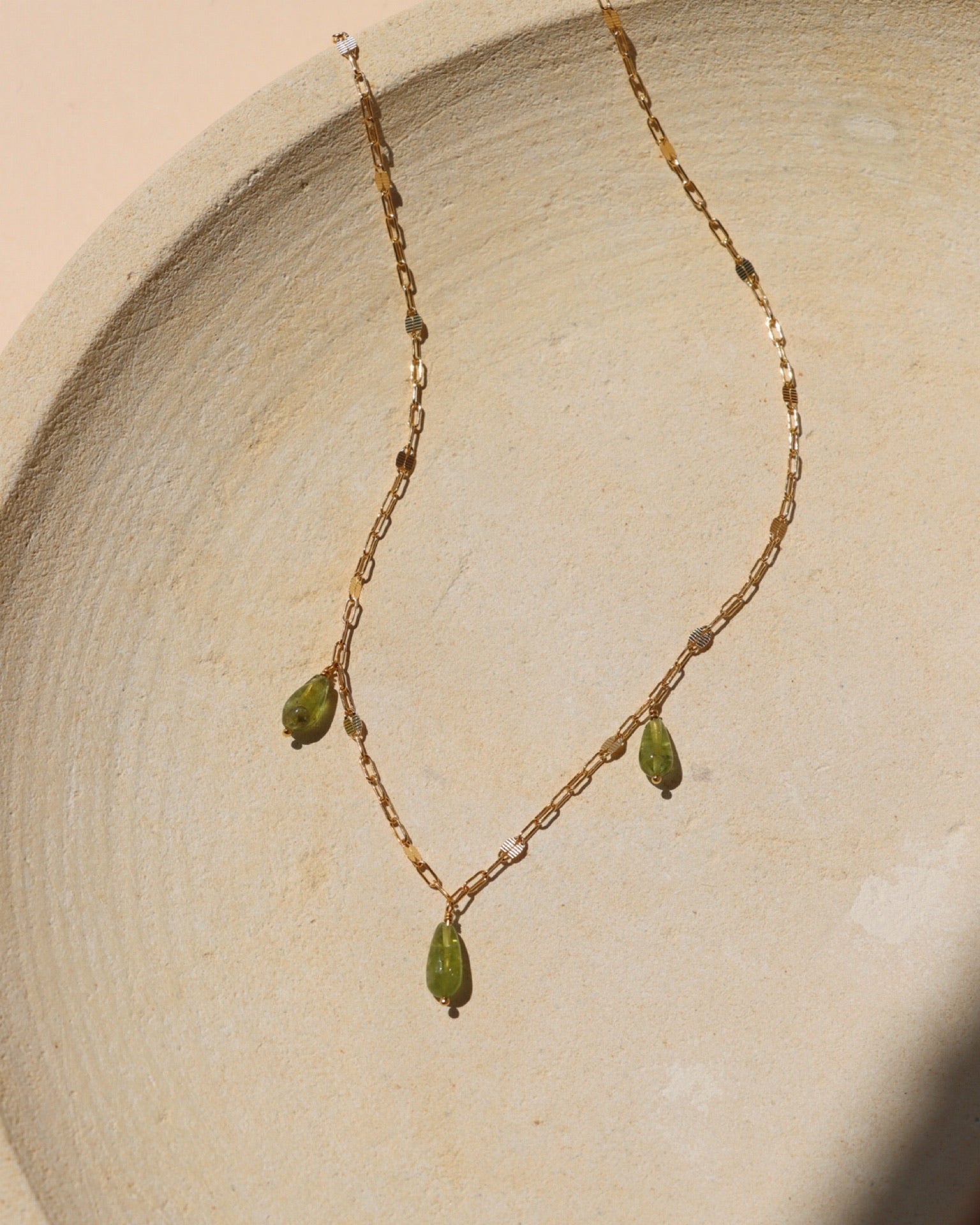 Peridot Charm Necklace featuring three natural green peridot gemstone charms on a 14k gold fill chain in warm sunlight.