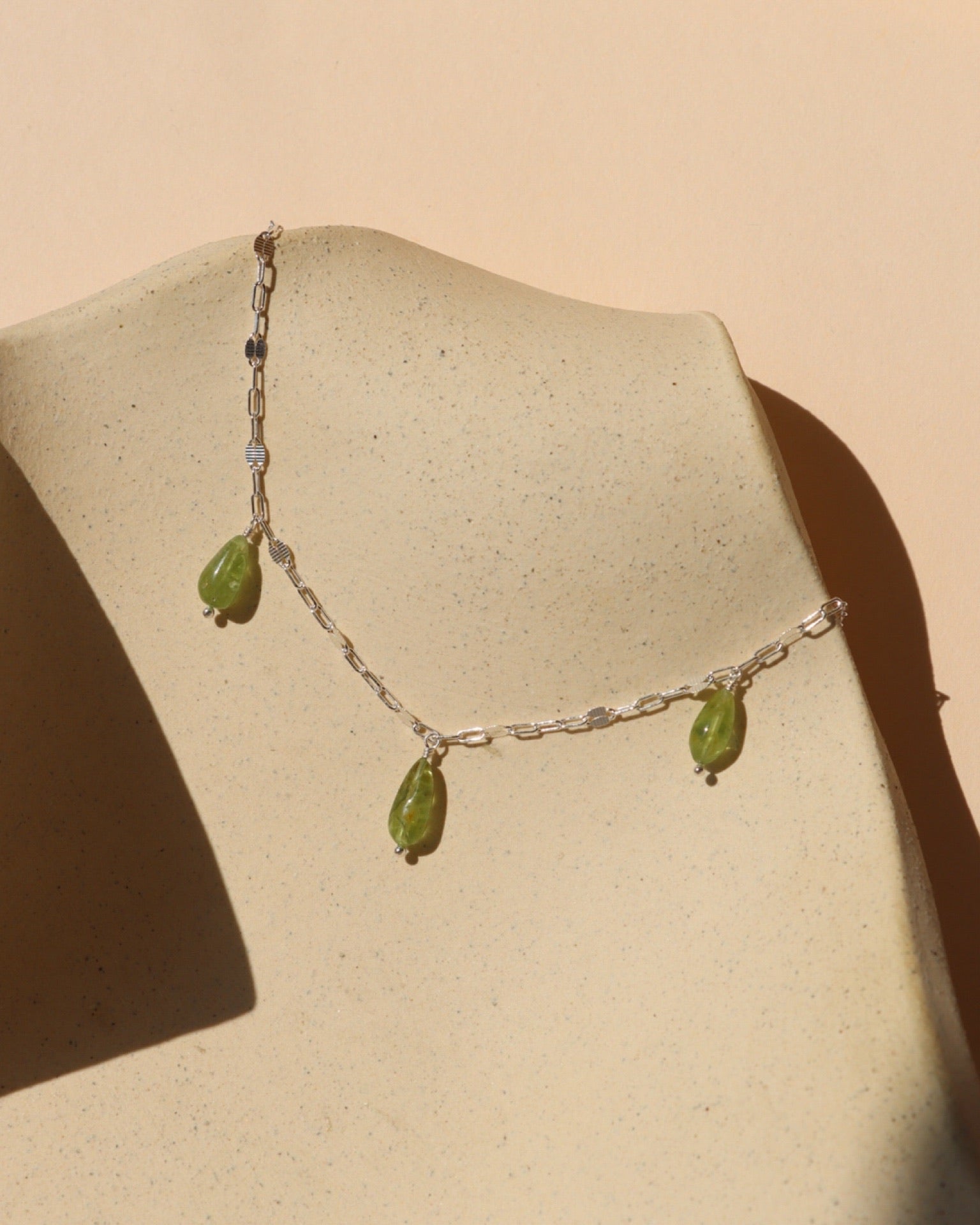 Sterling silver chain necklace with peridot stones on a light dish in the sunlight.