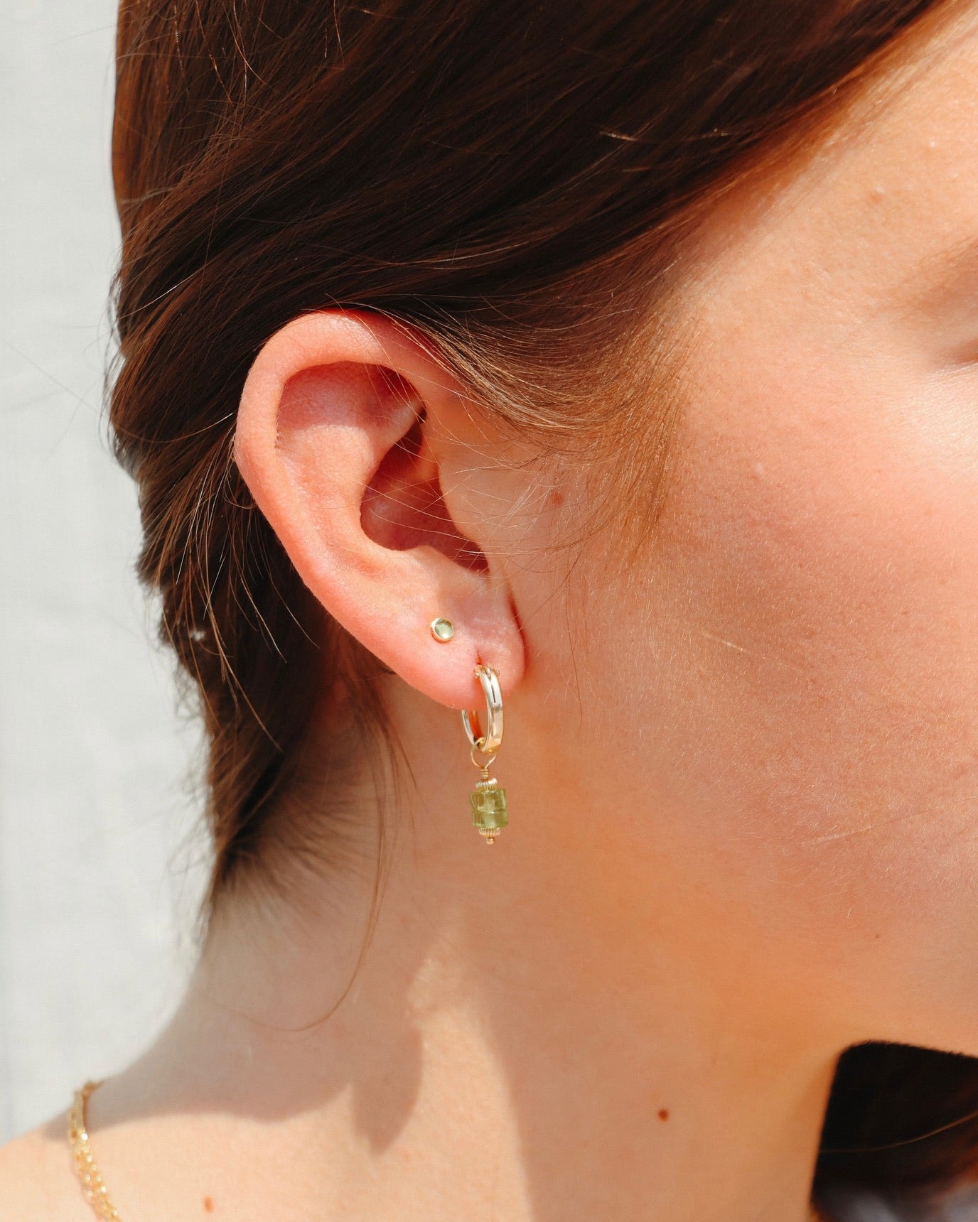 model wearing gold studs with peridot gemstones and gold hoops with peridot beads in the sunlight
