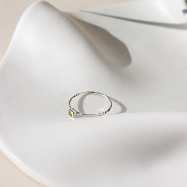 sterling silver band ring with 4mm peridot stone on a light dish