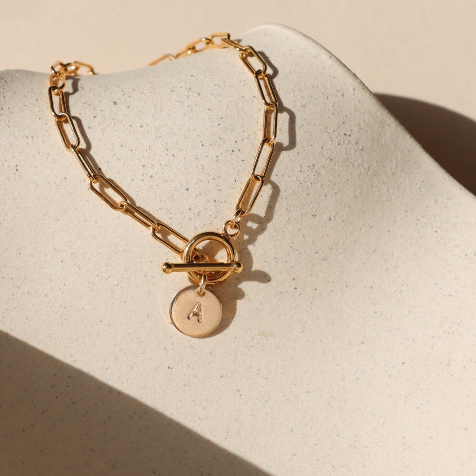 14k gold fill paperclip chain bracelet with toggle clasp & personalized stamp disc on a light dish