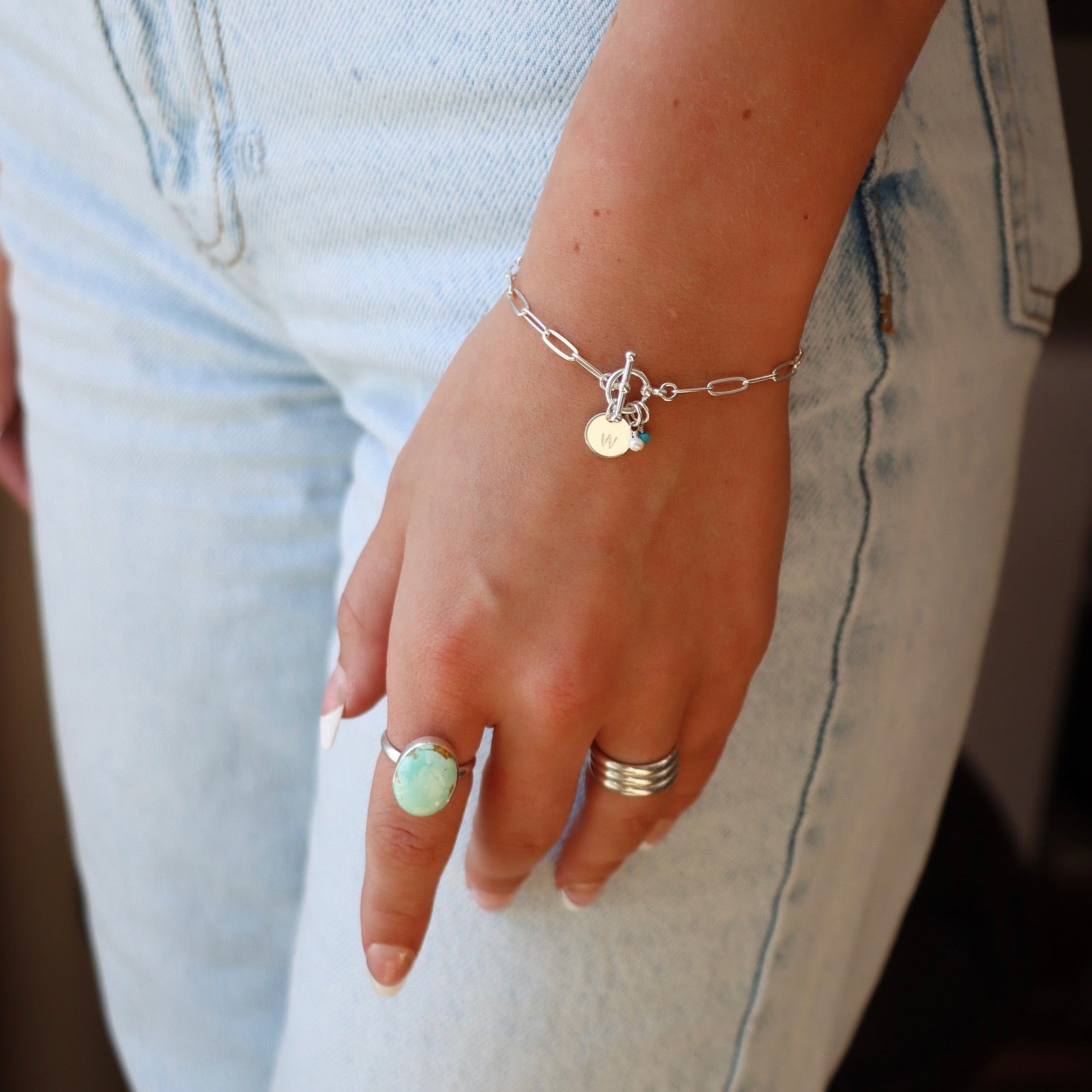 Close-up of a person's wrist wearing a bracelet and ring with light blue jeans.