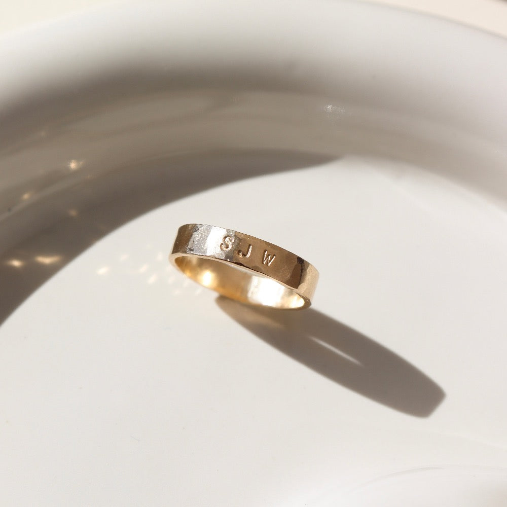 14k gold fill Initial stamped ring laid on a white plate in the sunlight. This ring features a hammered band that you get to customize with name or initials of your choice.