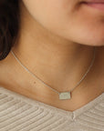 Model wearing sterling Silver necklace with a thin rolo chain with a silver smooth rectangle pendant with a "J" and a "T" stamped in the middle of it.