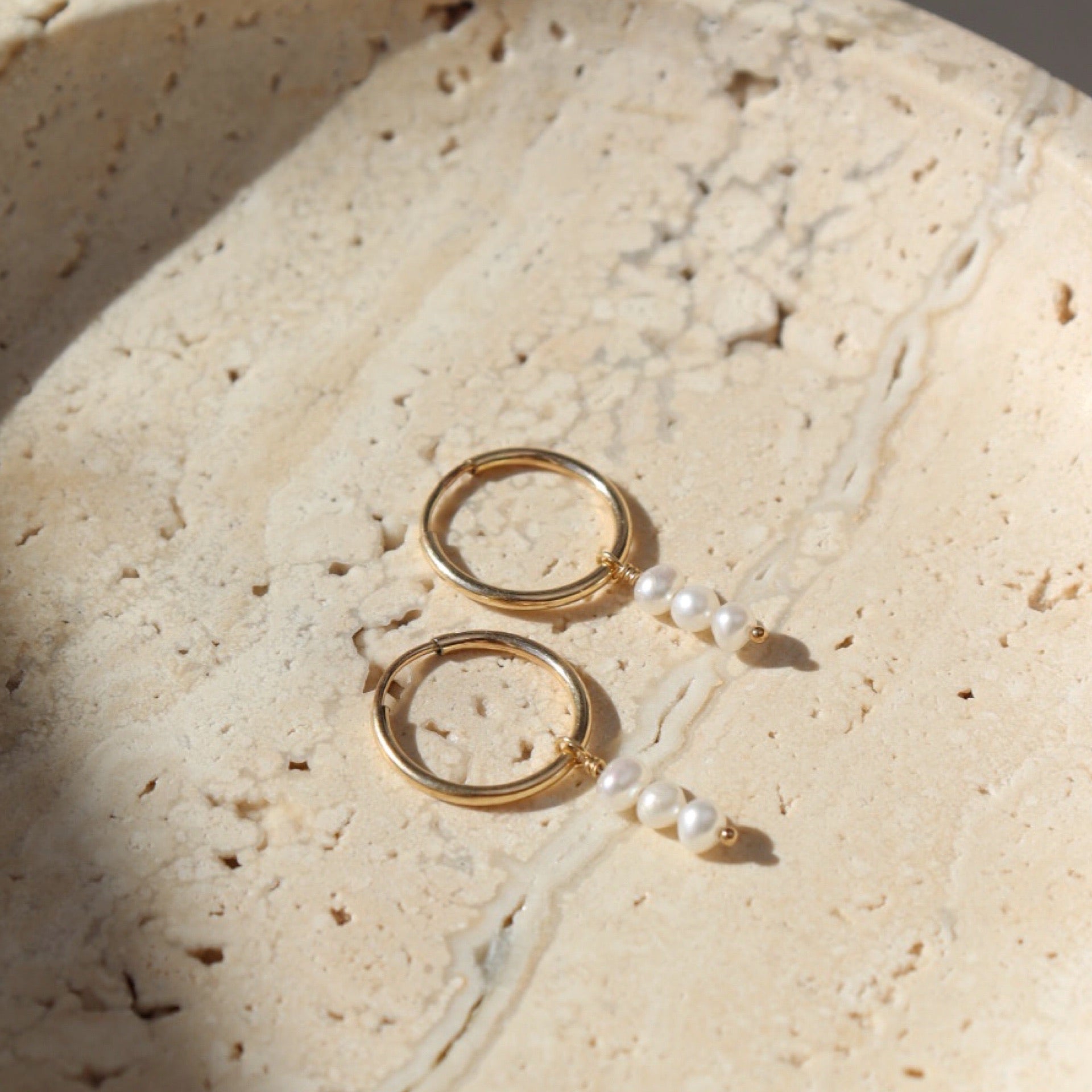 Gold petite hoops featuring three mini pearls hanging from each hoop. Earrings are displayed on a stone plate. 