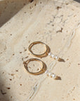 Gold petite hoops featuring three mini pearls hanging from each hoop. Earrings are displayed on a stone plate. 