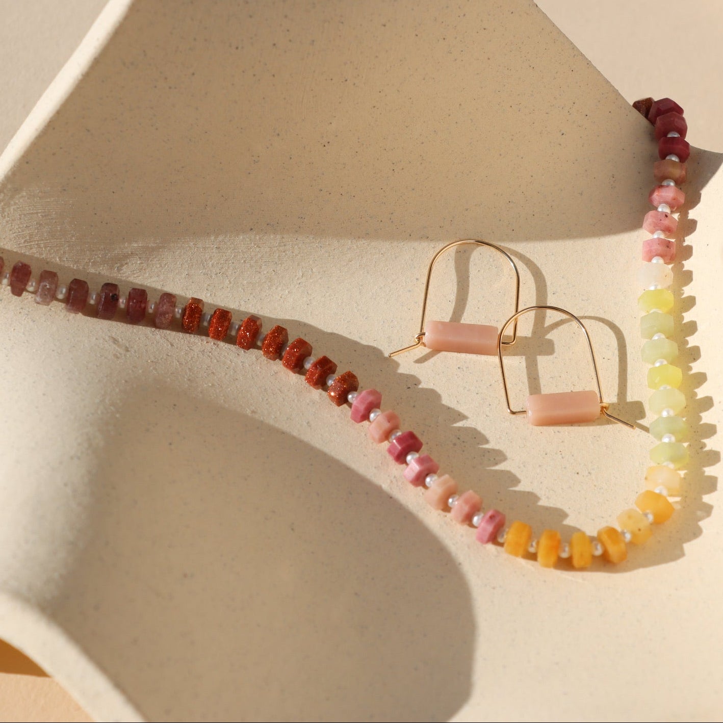 pink opal stones in 14k gold fill arch shaped earrings styled with multi colored stone bead and pearl neckalce in the sunlight
