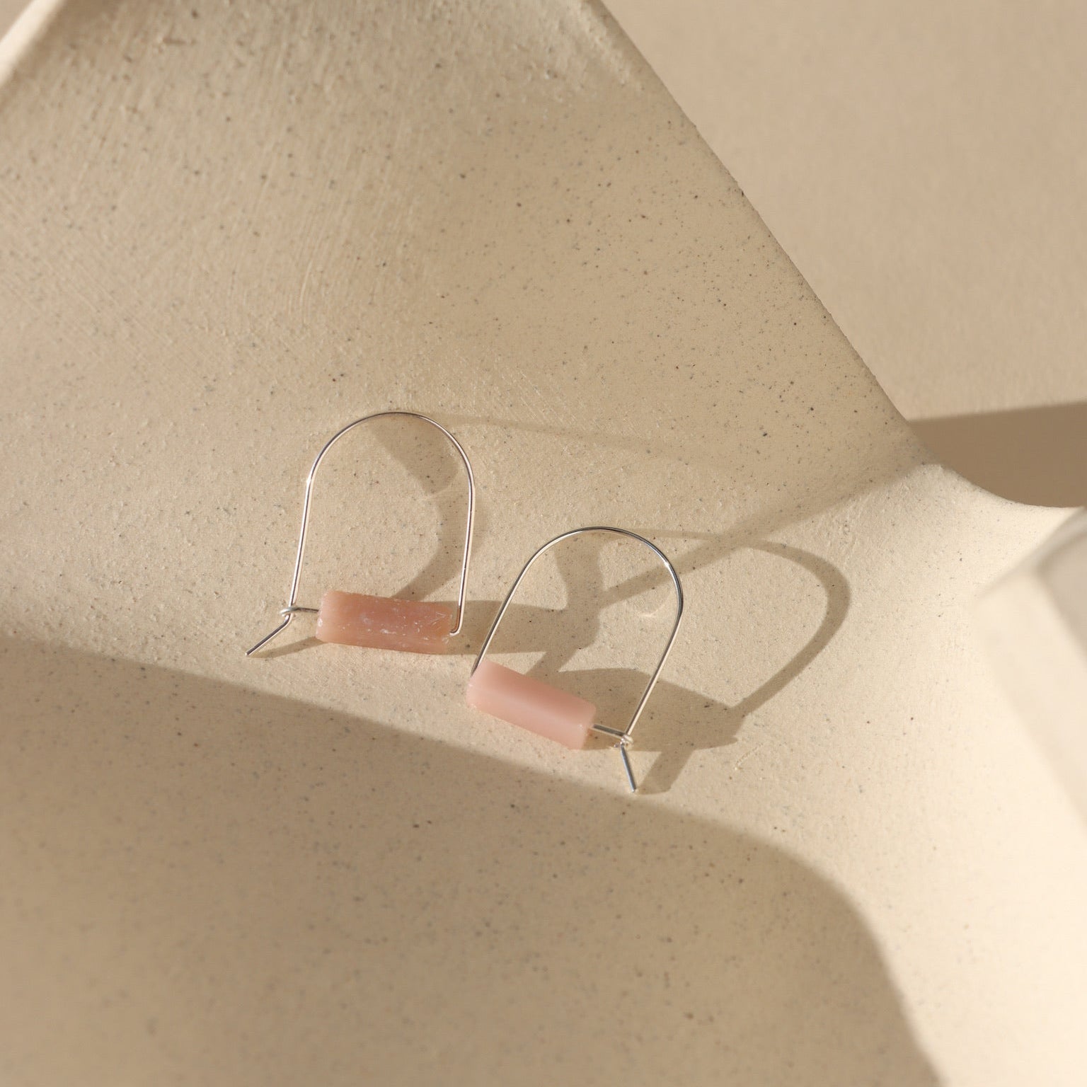 pink opal stones on sterling silver arch shaped earrings laid on light background in the sunlight