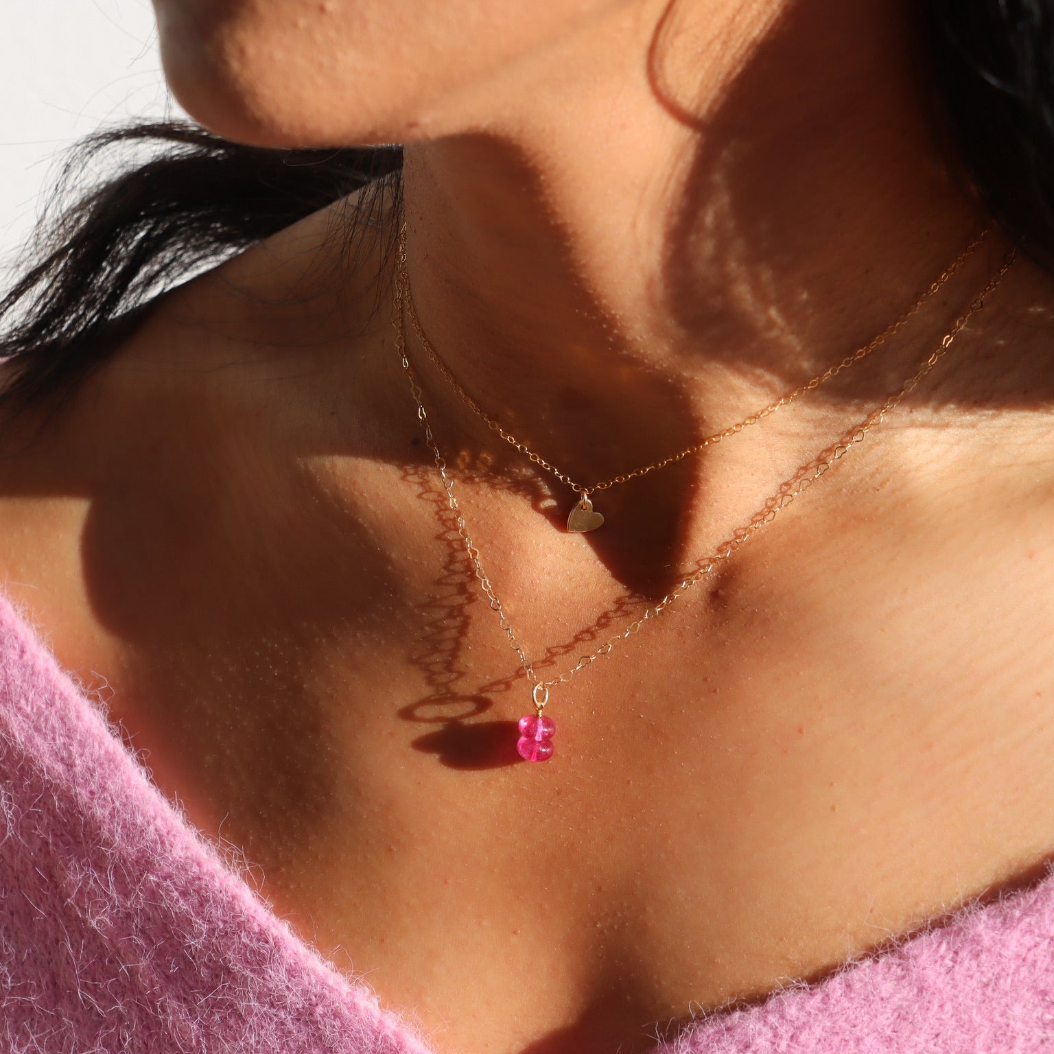 model wearing pink topaz charm in 14k gold fill on heart chain necklace layered with a heart charm necklace in 14k gold fill