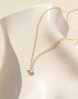 Delicate gold chain with a single pink pearl. Displayed on white dish. 