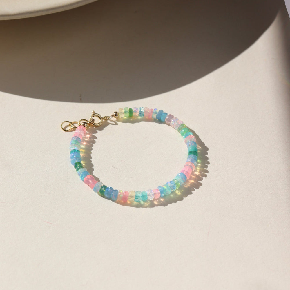 A vibrant colorful bracelet filled with a mix of different opal gemstones. This bracelet has a 14k gold fill standard clasp a 0.5" extender. Displayed on a cream backdrop. 