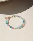 A vibrant colorful bracelet filled with a mix of different opal gemstones. This bracelet has a 14k gold fill standard clasp a 0.5" extender. Displayed on a cream backdrop. 