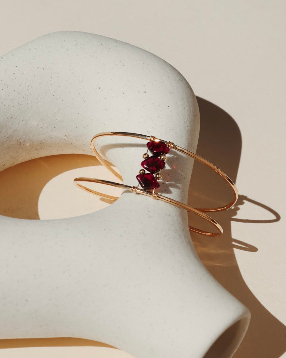 14k gold fill cuff bracelet with three ruby gemstones on a light dish