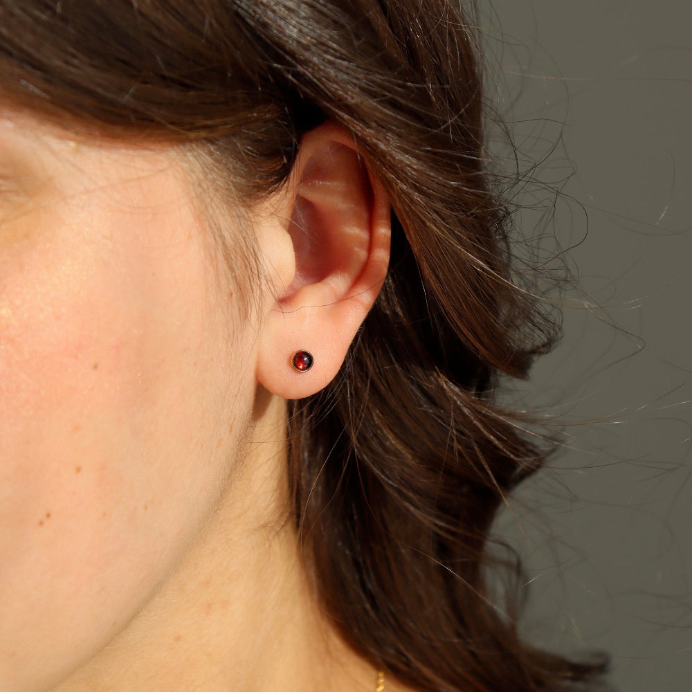 Model wearing a 14k gold fill red garnet stud. This stud features a 4mm red garnet gemstone. 