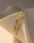 Remy chain drop earrings in gold with delicate chains and elongated accents, styled on a neutral sculptural surface.