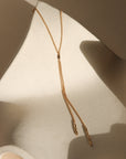 Remy chain lariat necklace in gold with a fine chain and elongated drop accents, styled on a sculptural neutral backdrop.