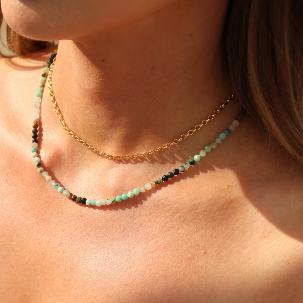 Model wearing 14k gold fill rolo styled chain stacked with a beaded gemstone necklace 