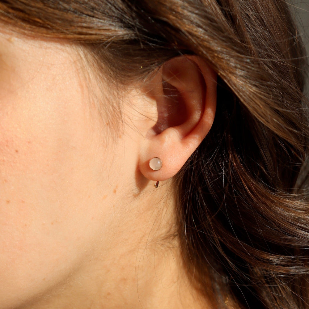 Rose quartz huggies in 14k gold fill taken on a model. These earrings feature a rose quartz stone on a thin gold wire that hugs the earlobe. 