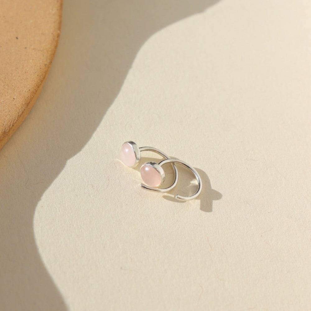 Our rose quartz Huggies feature a 5mm rose quartz gemstone. These earrings are made to hug your ear featuring a curved sterling silver post that will wrap around your ear. The earrings are on a white backdrop. 